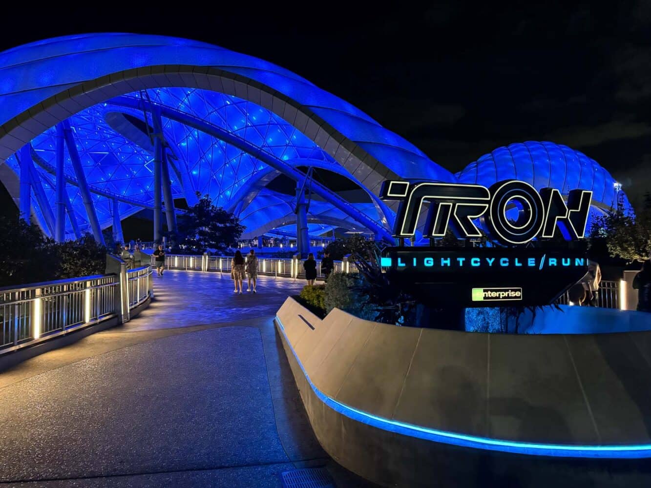 Sign at entrance for Tron Lightcycle Run ride and canopy lit up at night. 